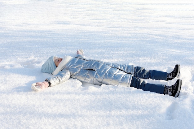 Foto giovane ragazza sdraiata sulla neve e godersi il momento della vita. giochi invernali all'aperto