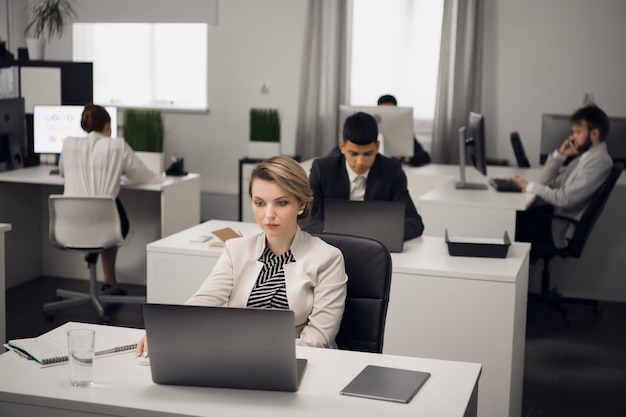 Una giovane ragazza manager in ufficio in un codice di abbigliamento da lavoro con un laptop comunica con un cliente dell'azienda.