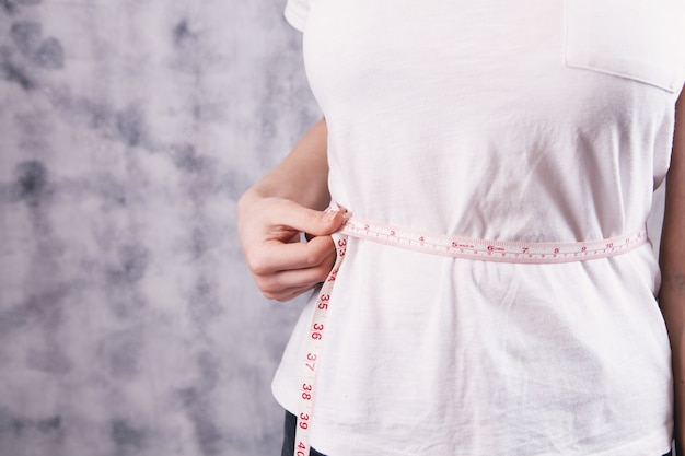 Young girl measures belly with a measuring tape