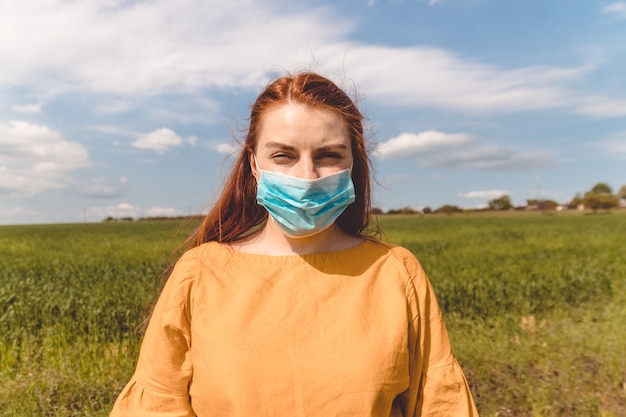 A young girl in a medical mask stands in a field