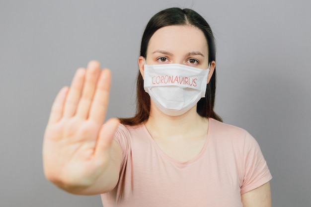 Молодая девушка в медицинской маске с текстом коронавируса на сером фоне. Пандемия, эпидемия в мире. Эмоции
