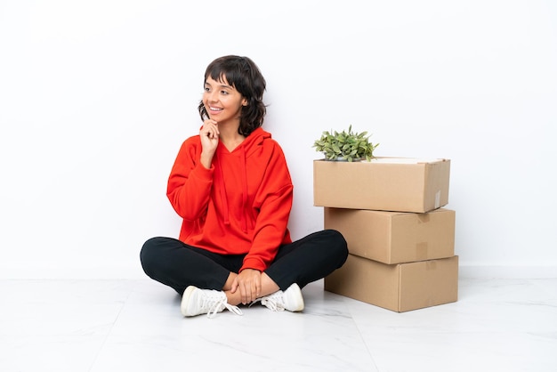 Young girl moving in new home among boxes isolated on white background looking to the side
