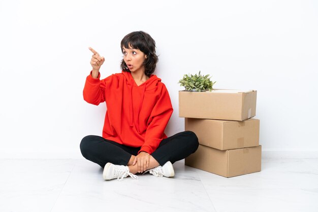 Young girl moving in new home among boxes isolated on white background pointing away