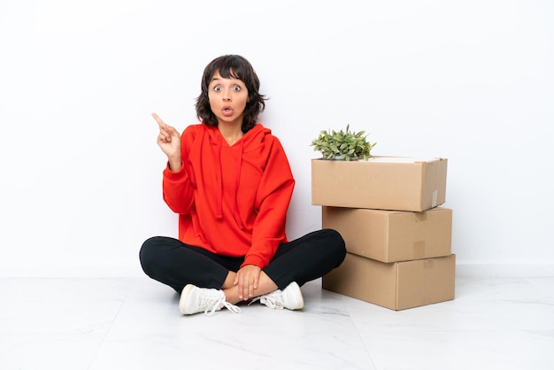 Young girl moving in new home among boxes isolated on white background surprised and pointing side
