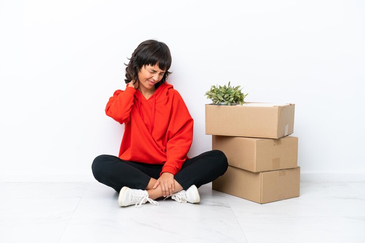 फोटो young girl moving in new home among boxes isolated on white background with neckache