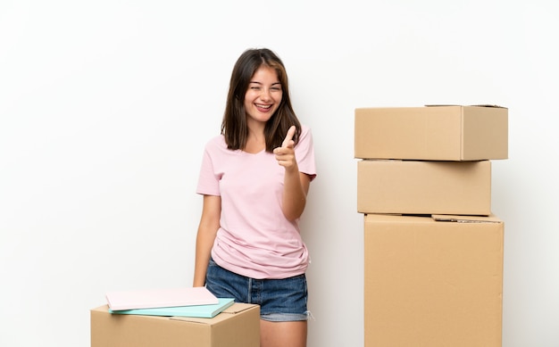 Young girl moving in new home among boxes points finger at you