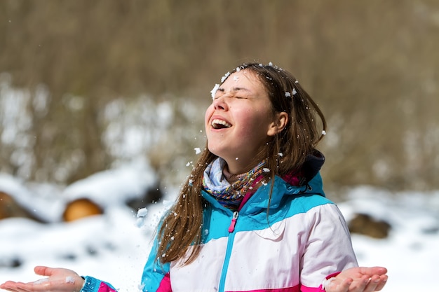 Foto una giovane ragazza con una giacca multicolore, con gli occhi chiusi, esulta per la neve che le cade sul viso