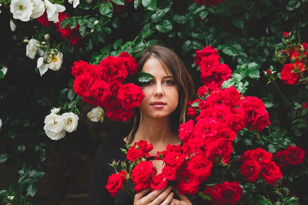 Giovane ragazza vicino al cespuglio di rose rosse e bianche