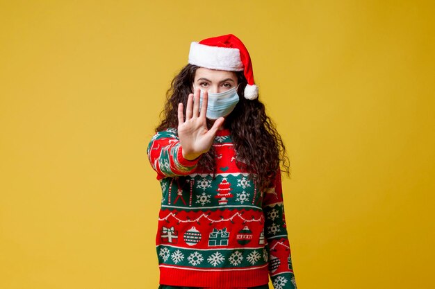 young girl in new year clothes and santa hat in medical protective mask shows gesture of refusal