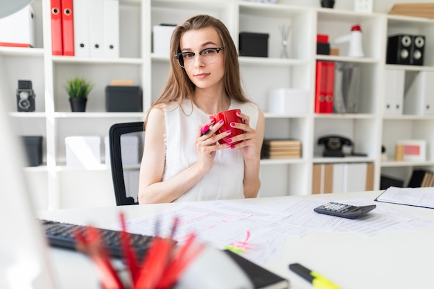 Una ragazza in ufficio tiene un pennarello rosa, una tazza rossa e lavora con i documenti.