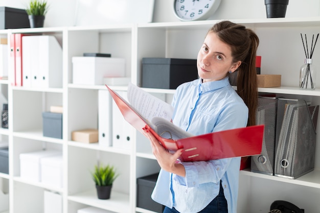 A young girl in the office is standing near the shelter and scrolls through the folder with the documents.