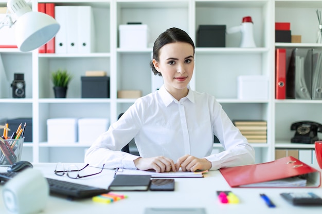 A young girl in the office sits at a table and holds a pen in her hands