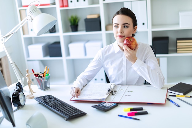 Young girl in the office working with documents and holding an apple.