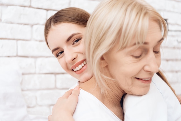 Young girl and old woman hugging in clinic together.