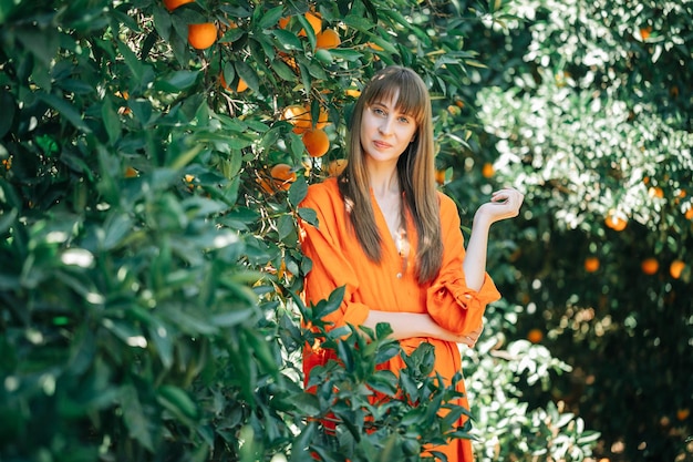 La ragazza in vestito arancione sta posando alla macchina fotografica nel giardino degli aranci