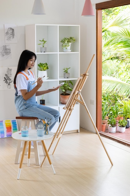 Молодая девушка рисует на бумаге дома в деревянной рамеХобби и изучение искусства дома