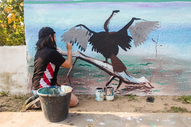 Young girl painting a wall with different colors in the street.