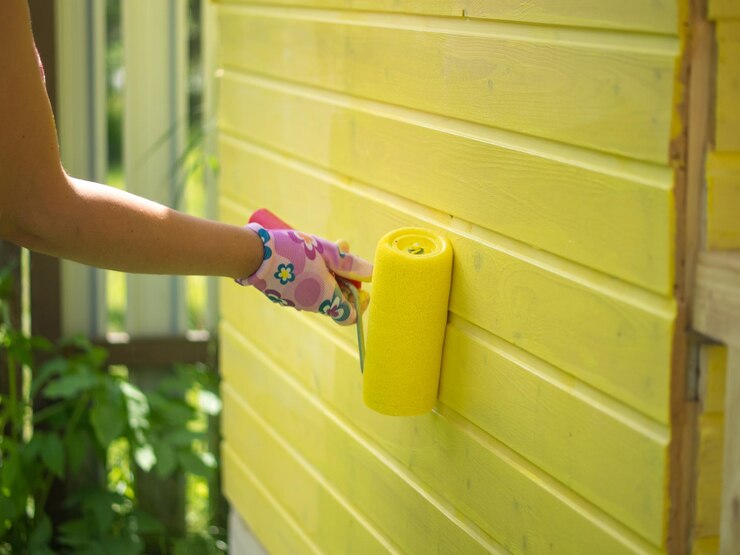 Young girl paints a wooden wall with a roller with yellow paint