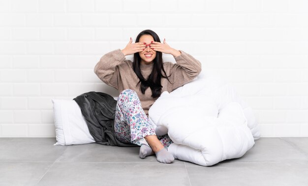 Young girl in pajamas at indoors covering eyes by hands