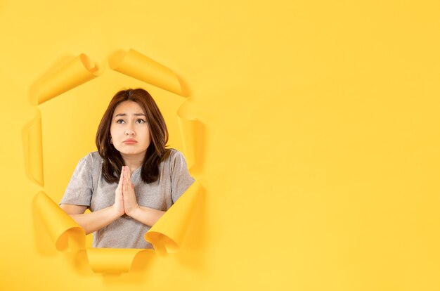 Photo young girl in pajamas looking through a hole in a yellow paper background window advertising