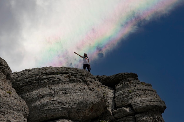 A young girl at the peak of a mountain and a rainbow in the sky