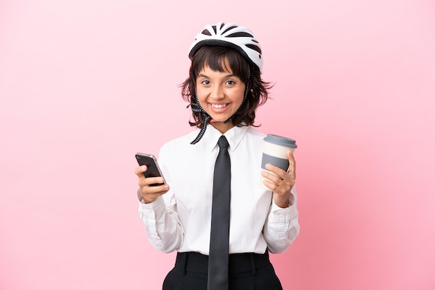 Young girl person with a bike helmet isolated on pink background holding coffee to take away and a mobile