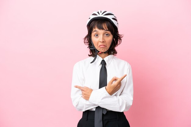 Young girl person with a bike helmet isolated on pink background pointing to the laterals having doubts
