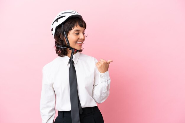 Young girl person with a bike helmet isolated on pink background pointing to the side to present a product