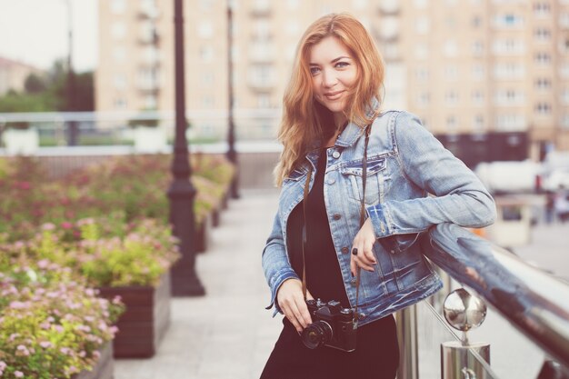 Young girl photographer walking along the street in a jeans jacket with an old camera