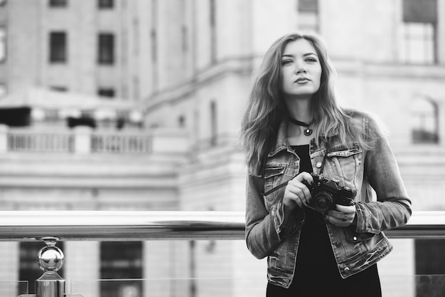 Fotografo di giovane ragazza che cammina lungo la strada in una giacca di jeans con una vecchia macchina fotografica