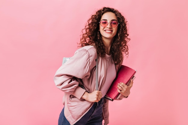 Young girl in pink jacket and sunglasses holding books on isolated background