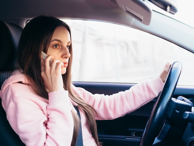 Young girl in pink pite speaks on the phone while sitting in a car.