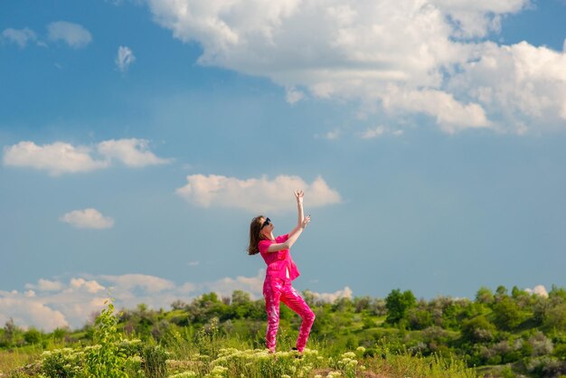 Young girl in pink posing in green grass in a field against a background of a cloudy sky