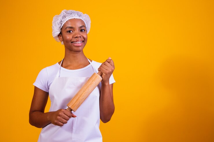 Young girl pizza maker on yellow background holding rolling pin.