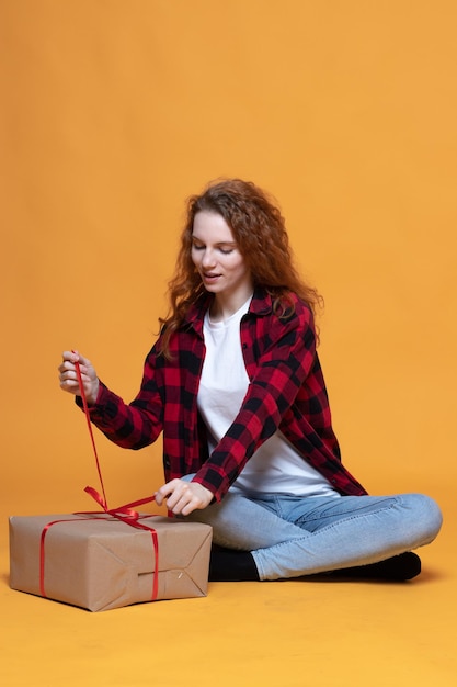 Foto ragazza in una camicia a quadri che tiene un regalo su uno sfondo arancione