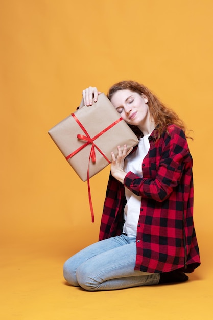 Young girl in a plaid shirt holding a gift on an orange background