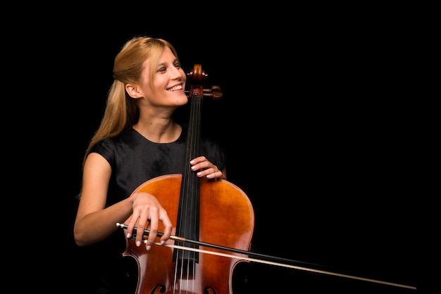 Young girl playing the cello on isolated black background