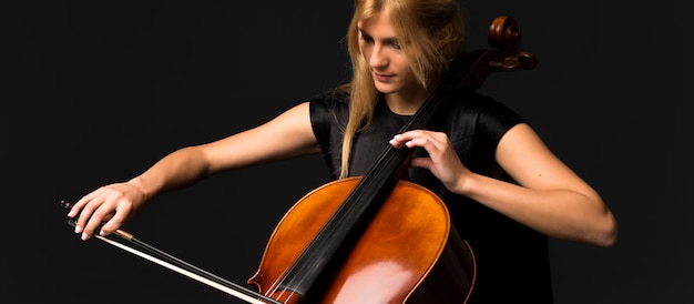 Молодая девушка играет на виолончели на черном фоне