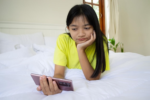 Молодая девушка играет в игру на смартфоне на кровати в спальне дома