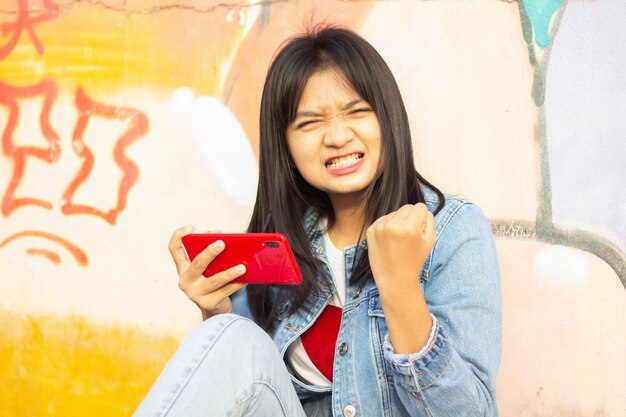 Молодая девушка играет в игру на смартфоне, сидя на красочном фоне