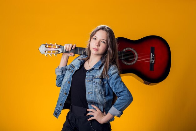 Young girl playing guitar on yellow background