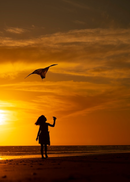 молодая девушка играет с воздушным змеем на пляже на закате