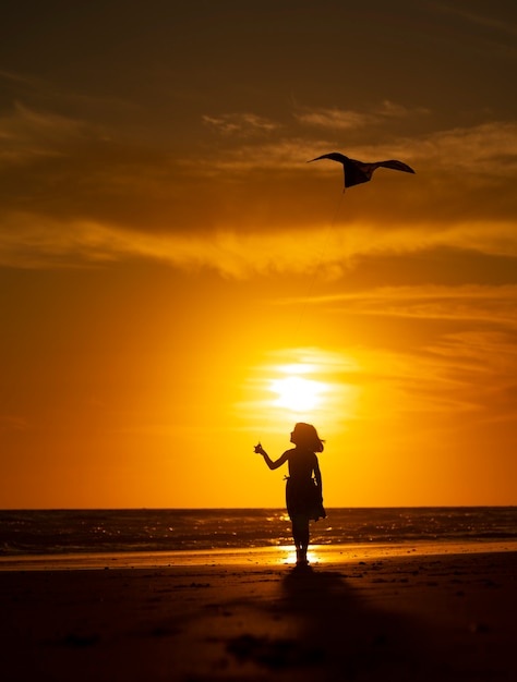 young girl playing with kite on the beach at sunset