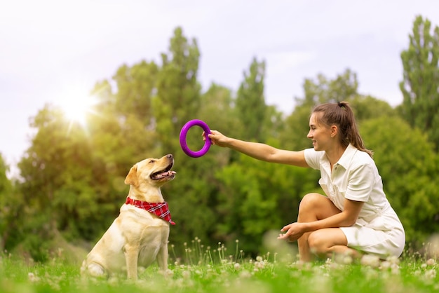 A young girl plays with a toy ring with a labrador dog on the grass