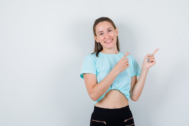 Young girl pointing up in turquoise t-shirt, pants and looking happy , front view.