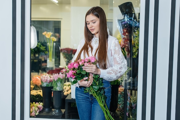 Una giovane ragazza posa con un bellissimo bouquet festivo sullo sfondo di un accogliente negozio di fiori fiorai e bouquet in un negozio di fiori piccole imprese