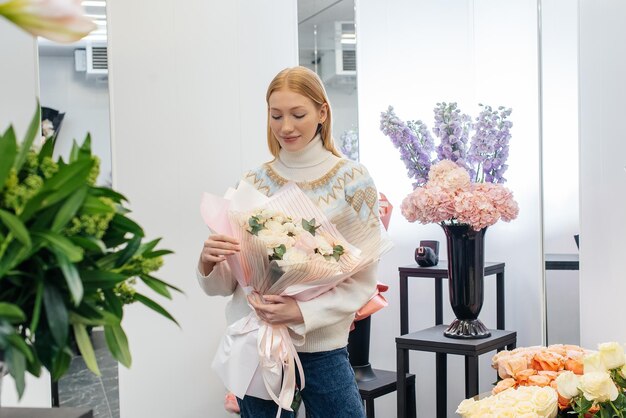 Una giovane ragazza posa con un bellissimo bouquet festivo sullo sfondo di un accogliente negozio di fiori fiorai e bouquet in un negozio di fiori piccole imprese