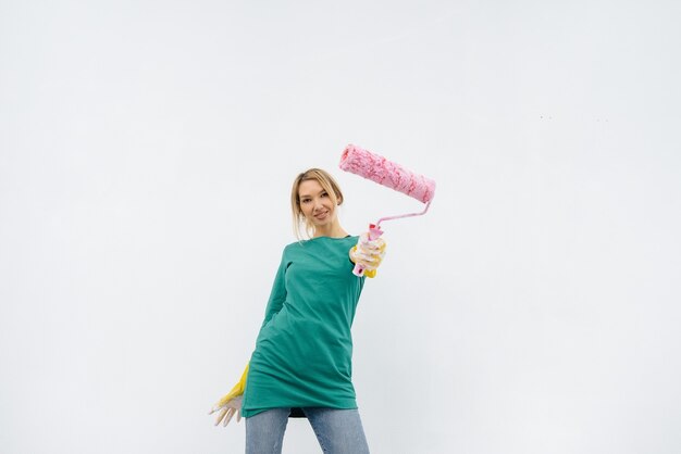 A young girl poses with a roller in front of a white wall. Repair of the interior.