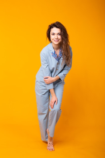 Young girl posing in pajamas on yellow wall. Relax good mood, lifestyle and sleepwear concept.