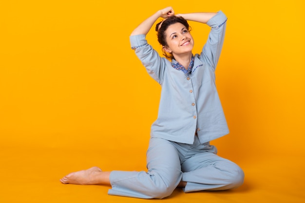 Young girl posing in pajamas on yellow wall. Relax good mood, lifestyle and sleepwear concept.